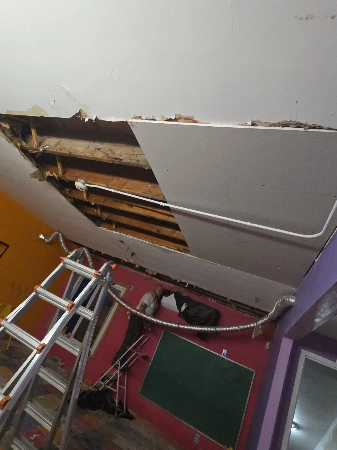 Opened ceiling showing framing and services above a ladder