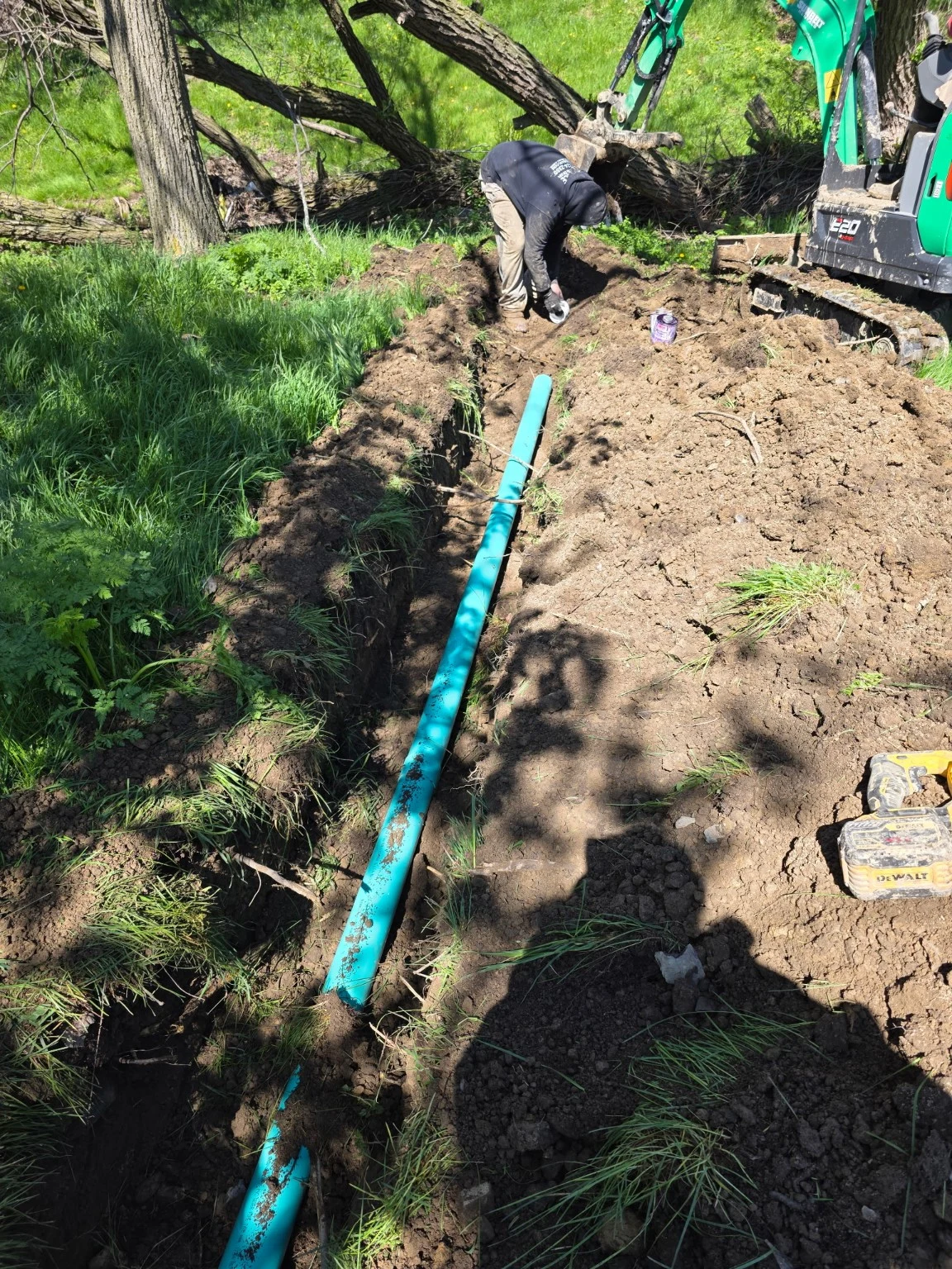 Worker beside an excavator with green pipe positioned in a trench